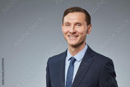 Portrait of smiling adult businessman looking at camera against plain grey background, copy space