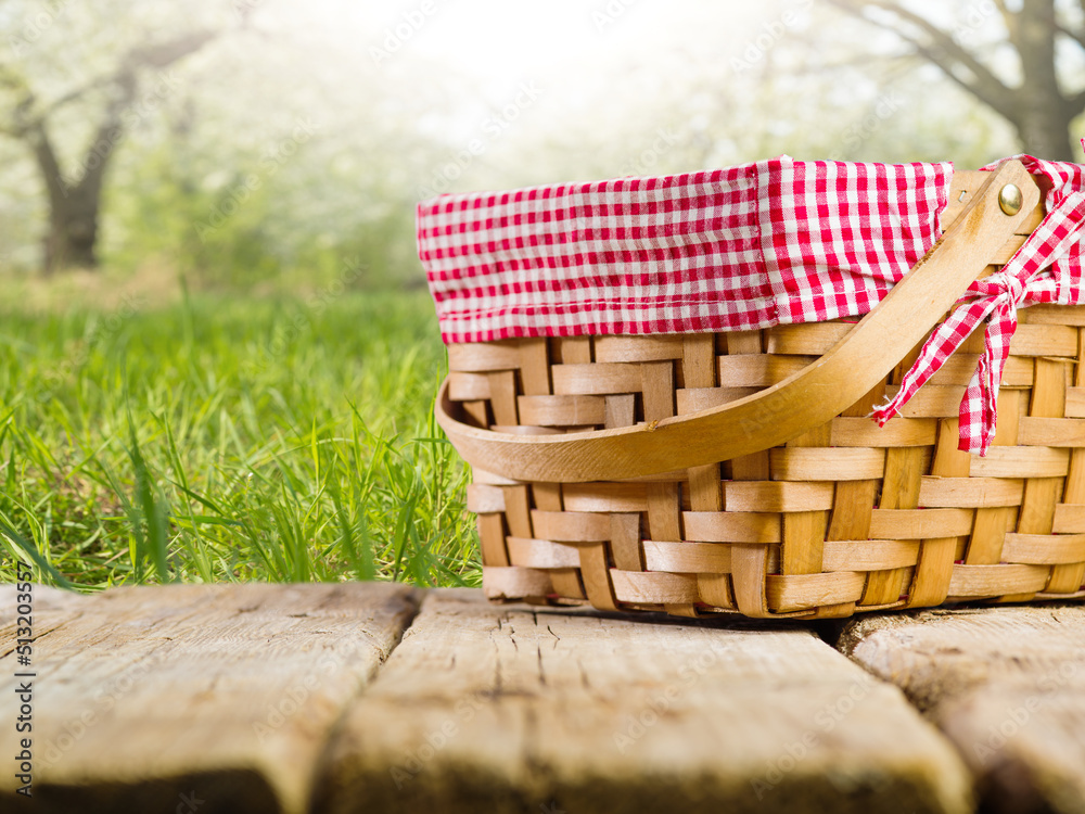 Obraz premium On a wooden table is a beautiful straw picnic basket against the backdrop of summer nature. Camping, picnic, healthy lifestyle, wholesome organic food, romance.