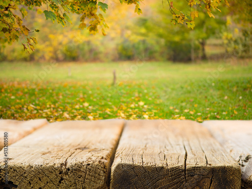 Against the background of a picturesque autumn background, a simple wooden table. The beauty of nature, golden autumn leaves fall on the green grass. Rest, picnic in nature. Thanksgiving Day.