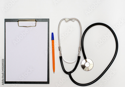 In the doctor's office, on the table is a stethoscope, a medical device for listening to the heartbeat, a tablet with a sheet of paper for recording, copy space