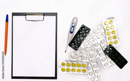 A universal tablet, a notebook for writing a prescription by a doctor, a medical thermometer and medicines on the table.