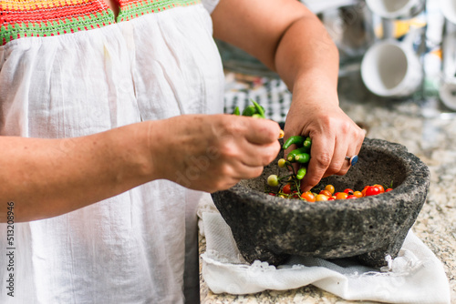 woman making mexican sauce in a stone molcajete with tomatoes and chilli peppers photo
