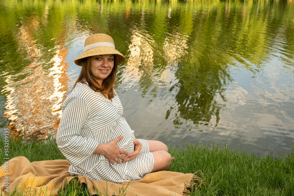 Beautiful pregnant young woman outside, relaxing and enjoying life in nature, warm sunny picture. Lovely couple near the pond. Maternity photoshoot. Young man standing with his pregnant woman