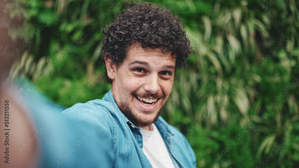 Close-up, young bearded man doing stream, video call on green leaves background Close-up, young bearded man doing stream, video call on green leaves background