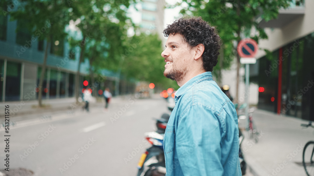 young bearded man in denim shirt smiling crossing the road at crosswalk on modern city background