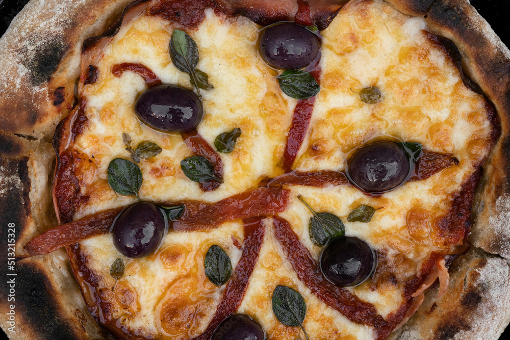 Pizza background. Closeup view of a pizza with mozzarella cheese, grilled red bell peppers, ham, black olives and fresh oregano leaves. Pizza background. Closeup view of a pizza with mozzarella cheese, grilled red bell peppers, ham, black olives and fresh oregano leaves.