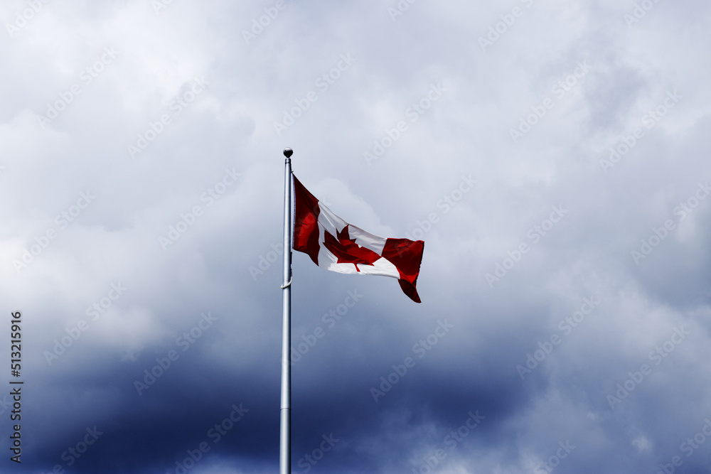 Canadian flag on a flagpole with a dramatic clouds Canadian flag on a flagpole with a dramatic clouds