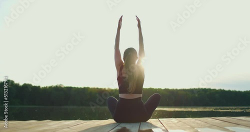 Young woman does yoga on the shore oflake in the fresh air. Rear view. Slow motion photo