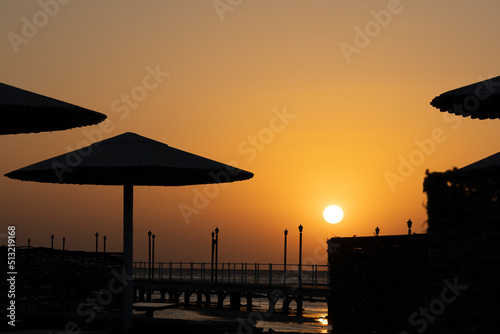 Beautiful sunrise with clear sky on the beach in Hurghada. No people, wooden water umbrellas. Sun reflection in the Red Sea water. © DriveAndDive