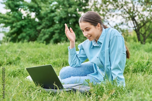 Teenage girl high school student using laptop while sitting on green grass