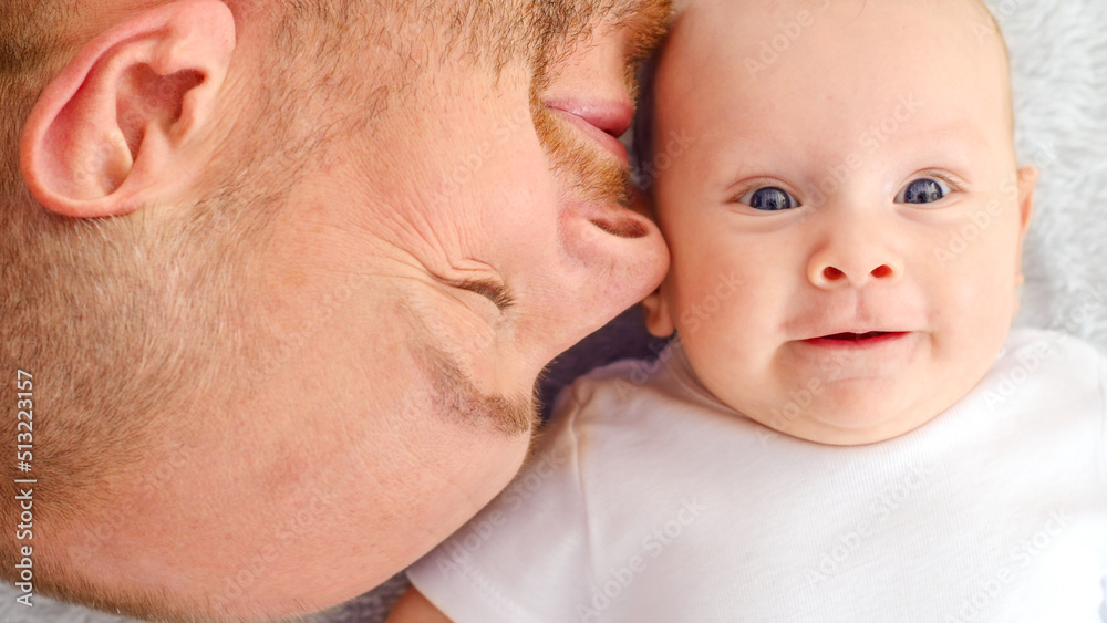 Happy newborn baby with his dad. Healthy newborn baby in a white t-shirt with father. Closeup Faces of the daddy and infant baby. Cute Infant boy and parent, top view. Happy family Happy newborn baby with his dad. Healthy newborn baby in a white t-shirt with father. Closeup Faces of the daddy and infant baby. Cute Infant boy and parent, top view. Happy family