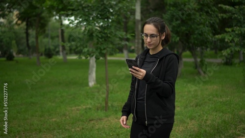 A young woman is jogging with her phone in the park. Asian girl with glasses running with app in phone move to earn. photo