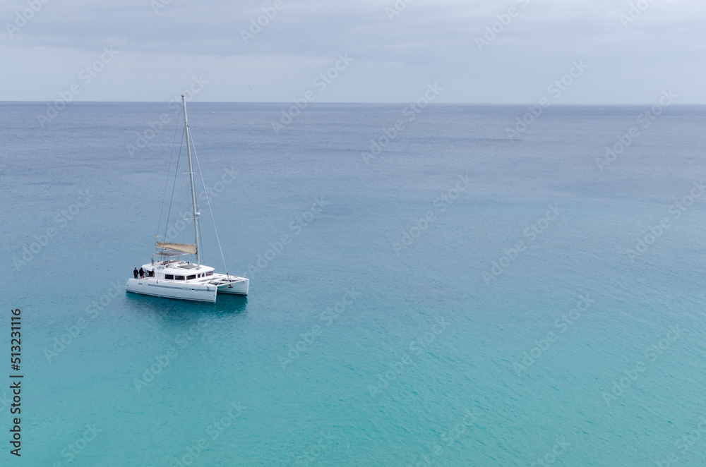 family cruising on a catamaran on the calm turquoise sea. group of tourists on the mediterranean sea in the canary islands. single catamaran sailing in the turquoise ocean. family cruising on a catamaran on the calm turquoise sea. group of tourists on the mediterranean sea in the canary islands. single catamaran sailing in the turquoise ocean.