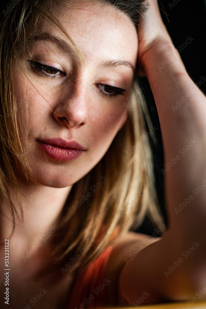 Fototapeta premium A contemplative young female model in natural makeup. Studio close head and shoulder portrait of a beautiful woman set against a black background.