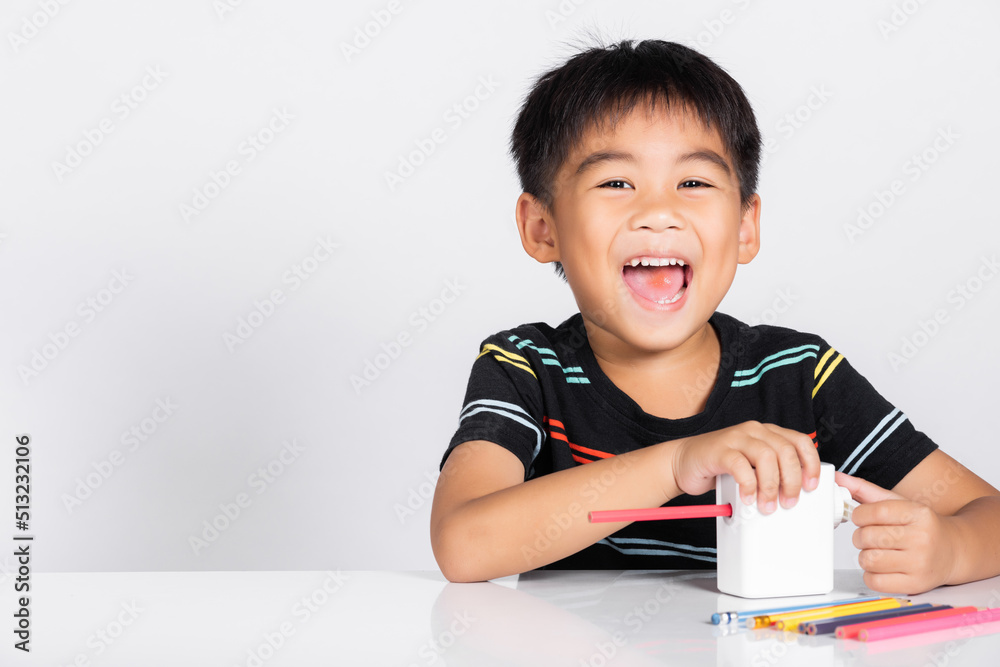 Fototapeta premium Little cute kid boy 5-6 years old smile using pencil sharpener while doing homework in studio shot isolated on white background, Asian children preschool sharpening color pencils, education concept