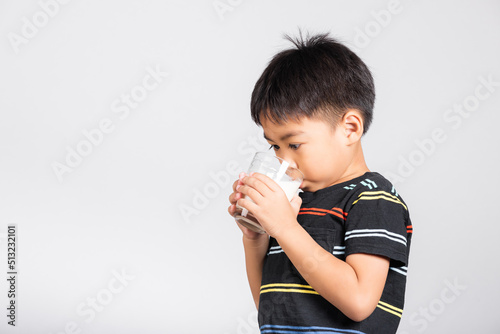 Little cute kid boy 5-6 years old smile holding milk glass he drinking white milk in studio shot isolated on white background, Asian children preschool, Daily life health care Medicine food