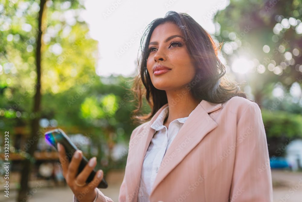Beautiful young Latin woman using smartphone standing on city street. Portrait of Latina smiling female using mobile phone. Beautiful young Latin woman using smartphone standing on city street. Portrait of Latina smiling female using mobile phone.