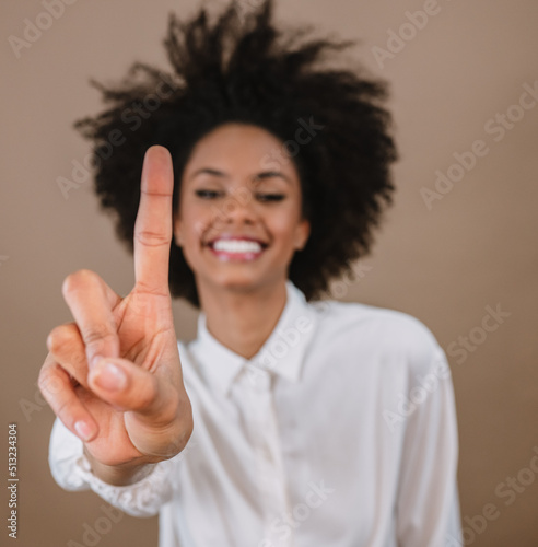 Smiling Latin woman making one, first countdown times sign gesture with hand fingers on pastel background.