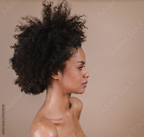 Side a smiling young Latin afro woman. Joy, positive and love. Beautiful african-style hair. Pastel studio background.