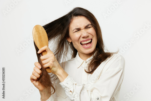 a brunette tries to comb her long hair with a wooden comb and screams in pain. Horizontal photo on a light background with empty space