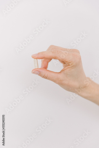 A single white pill being held by a women on a white backdrop.