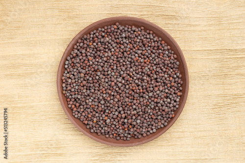 Spice Mustard seeds (Brassica juncea) in brown clay plate on wooden background. Close up. Vegetarian food concept