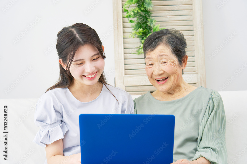 リビングでノートパソコンを使う孫と祖母 リビングでノートパソコンを使う孫と祖母