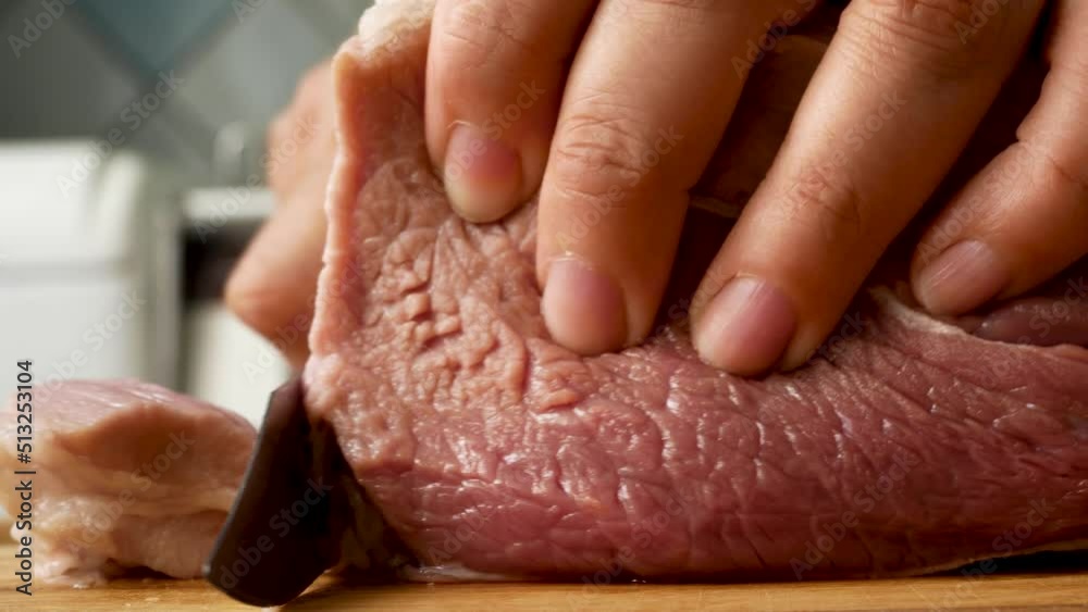 Female hands cut raw pork meat with a knife on a wooden board in the kitchen. Cooking meat dishes
