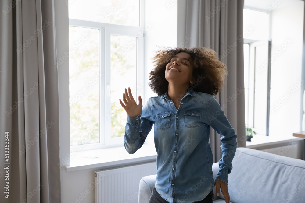 Happy teenage curly-haired African girl dancing alone at home looks untroubled moves to favourite song listen cool music enjoy carefree weekend spend time in living room. Hobby, leisure, fun concept Happy teenage curly-haired African girl dancing alone at home looks untroubled moves to favourite song listen cool music enjoy carefree weekend spend time in living room. Hobby, leisure, fun concept