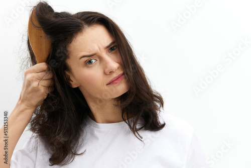 a sad, upset woman is trying to comb her long, dark, tangled hair with a wooden massage comb with a very sad, sad face