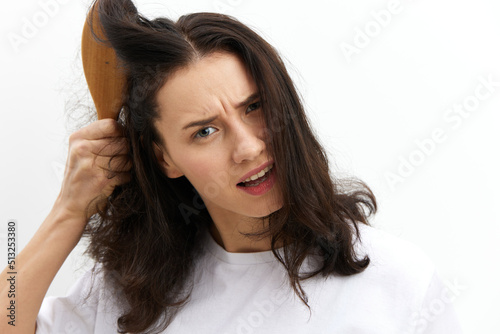 a sad, upset woman is trying to comb her long, dark, tangled hair with a wooden massage comb with a very sad, sad face
