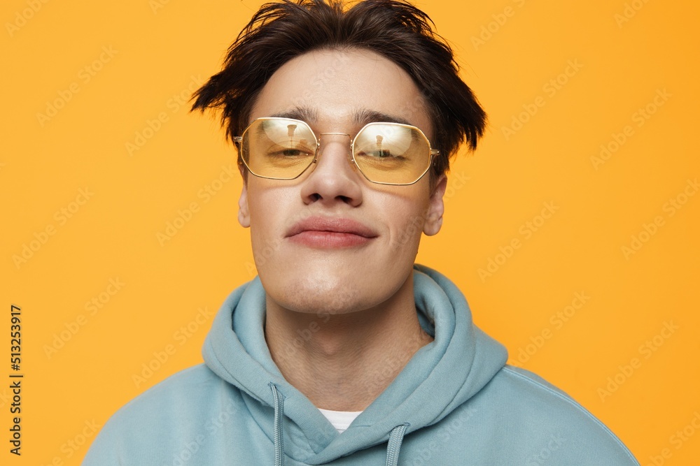 a close portrait of a funny man standing on an orange background in bright sunglasses looking at the camera with a smile