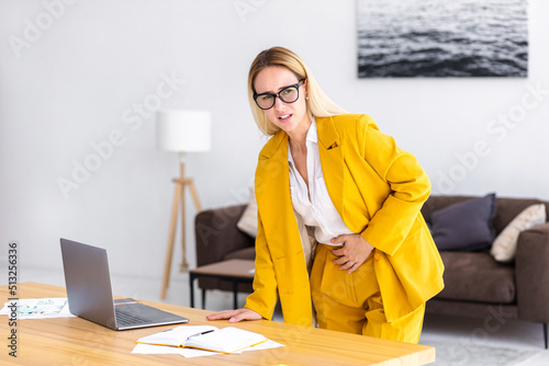 Young woman employee leaning on the table suffering from stomach pain standing in the office