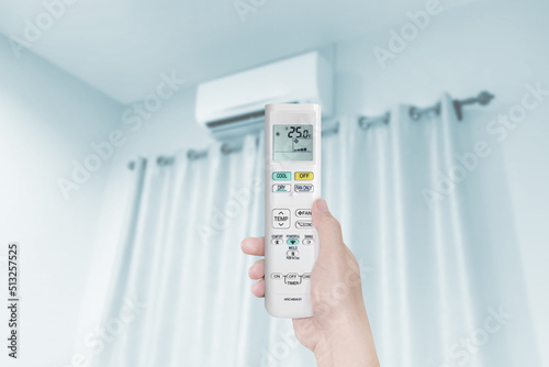 woman holding air conditioner remote control with air conditioner in blue bedroom