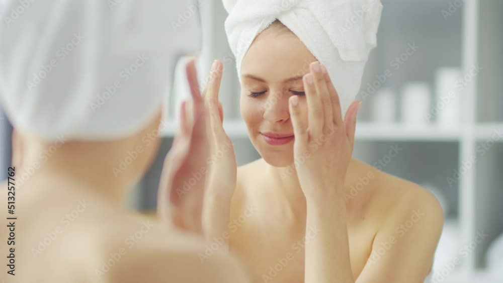 Young Girl is Sitting in front of a Make-up Mirror in the Bathroom and Applying a Skin Cream. Beautiful Woman is Making Cosmetic Rejuvenation Procedures. Health and Beauty Concept. Young Girl is Sitting in front of a Make-up Mirror in the Bathroom and Applying a Skin Cream. Beautiful Woman is Making Cosmetic Rejuvenation Procedures. Health and Beauty Concept.