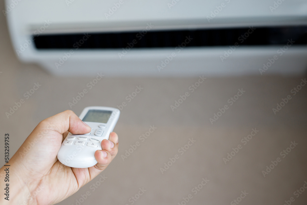 Air conditioner inside the room with close up man hand holding using directed operating remote controller.