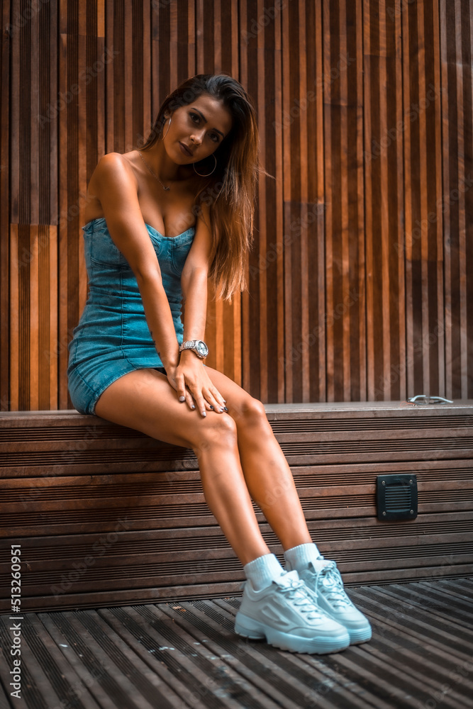 Portrait of a pretty brunette girl sitting on a wooden chair in a denim skirt Portrait of a pretty brunette girl sitting on a wooden chair in a denim skirt