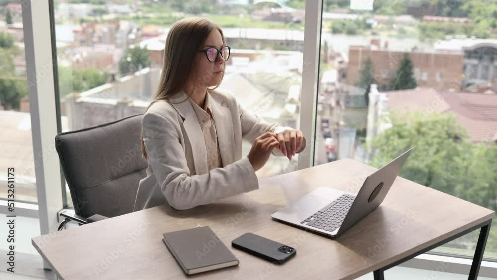 A young successful woman in glasses sits relaxed at her desk, the end of the working day in the office. Woman in classic business clothes A young successful woman in glasses sits relaxed at her desk, the end of the working day in the office. Woman in classic business clothes