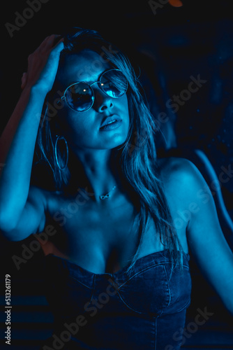 Brunette model at night in the city with blue leds, blue glasses in a dark glass