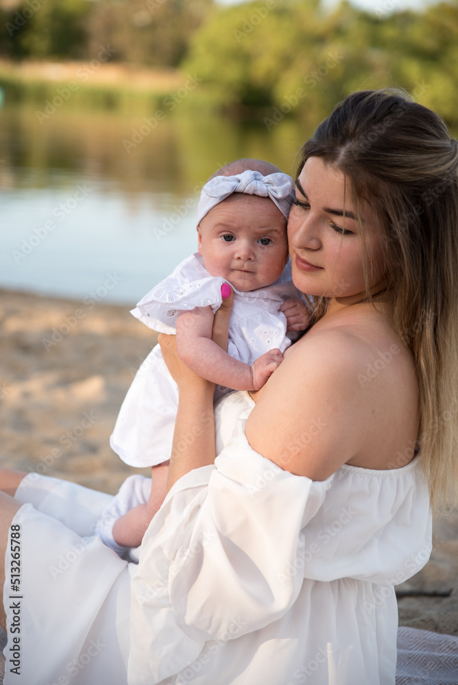 Fototapeta premium mom with a newborn baby sits on the beach, on the sand. mom holds a newborn baby in her arms.