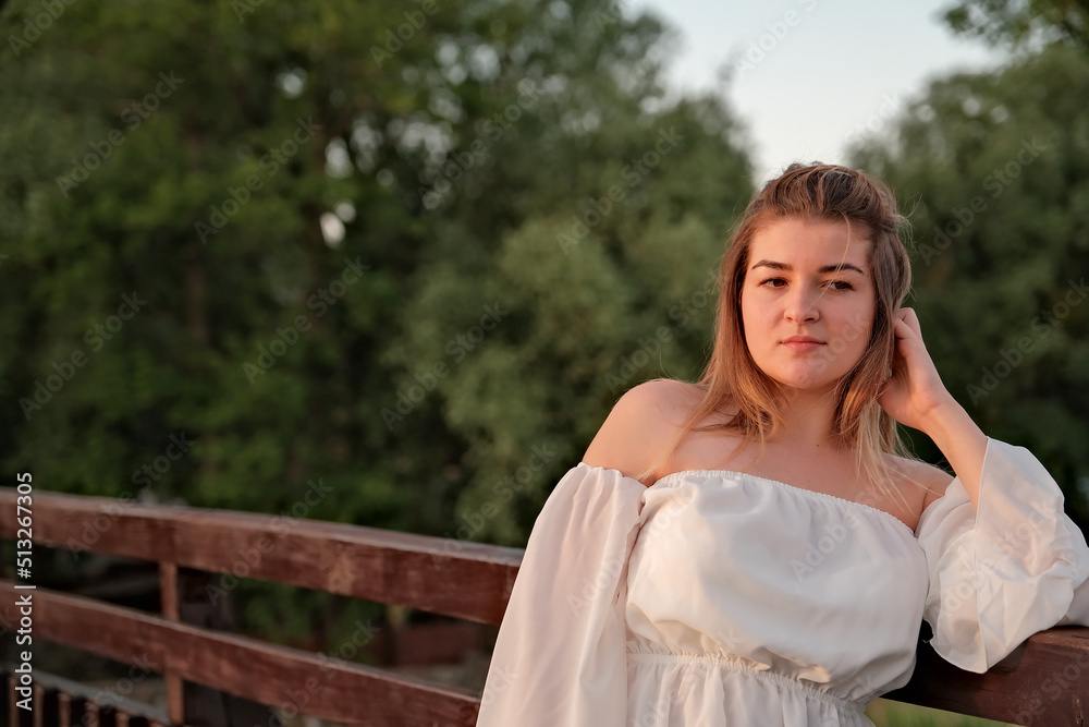 a beautiful girl in a white dress stands on a wooden bridge. a beautiful girl in a white dress stands on a wooden bridge.