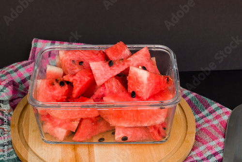 Sliced watermelon in glass container with black seeds on black background 