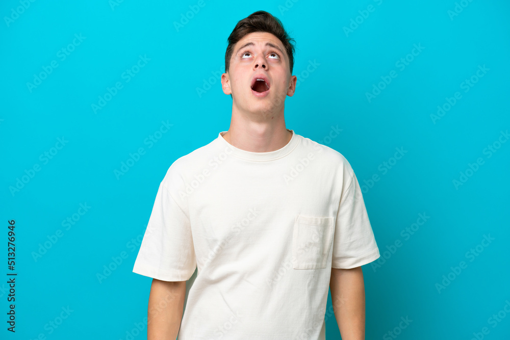Young handsome Brazilian man isolated on blue background looking up and with surprised expression Young handsome Brazilian man isolated on blue background looking up and with surprised expression