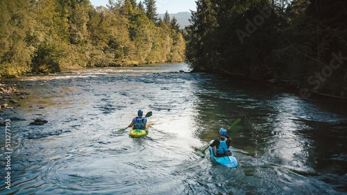 Two men in kayaks  paddling over a mountain river  enjoying the view of beautiful green forest coast  aerial tracking shot.