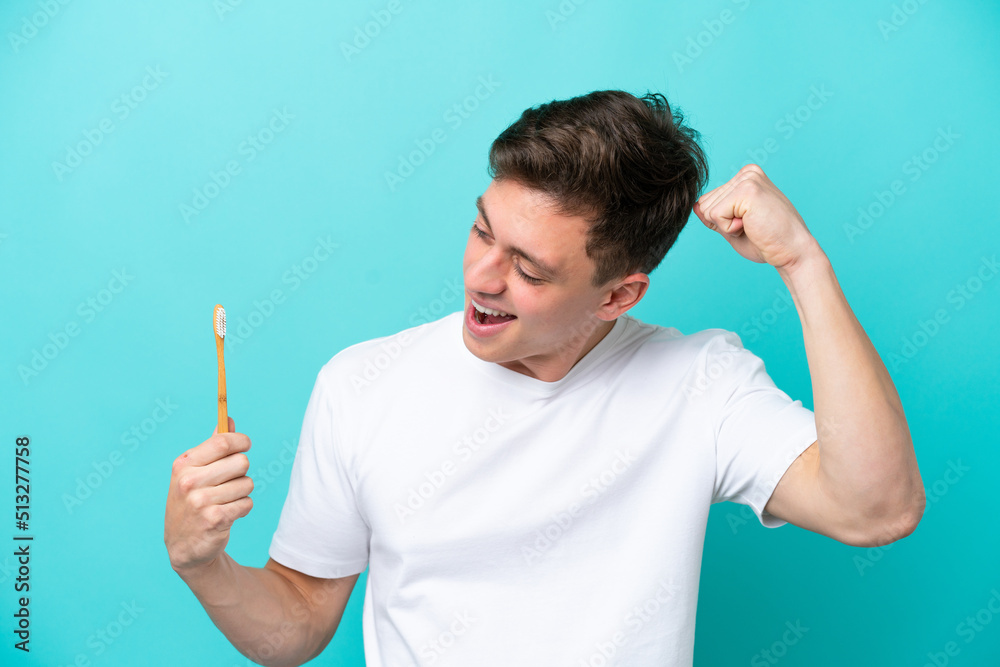 Young Brazilian man brushing teeth isolated on blue background celebrating a victory Young Brazilian man brushing teeth isolated on blue background celebrating a victory
