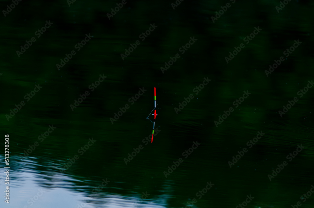 Fishing float in blue water. The float floats on the water surface of a lake, river. Stock Photo