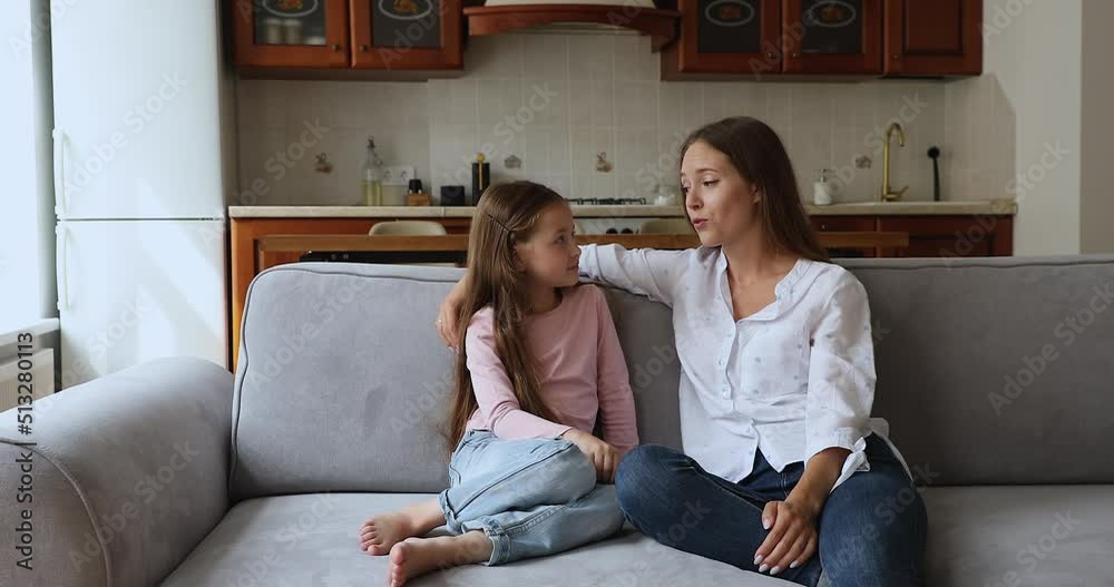 Happy loving mom and little daughter kid talking at home, smiling, sitting on home couch, enjoying conversation, discussion. Mother, counselor answering child questions. Motherhood concept