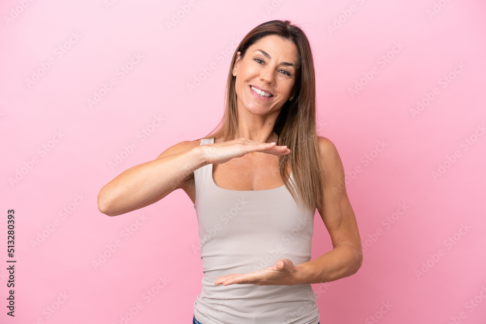 Middle age caucasian woman isolated on pink background holding copyspace imaginary on the palm to insert an ad Middle age caucasian woman isolated on pink background holding copyspace imaginary on the palm to insert an ad
