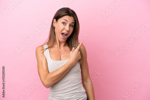 Middle age caucasian woman isolated on pink background surprised and pointing side