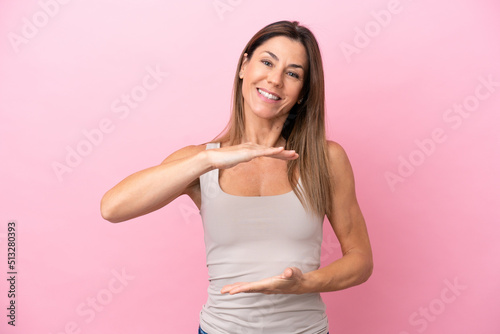 Middle age caucasian woman isolated on pink background holding copyspace imaginary on the palm to insert an ad © luismolinero